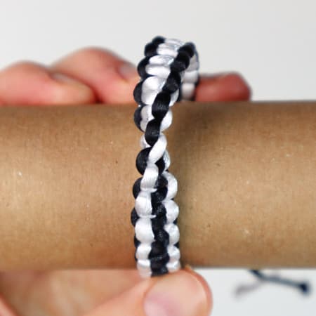 Two-color macrame bracelet close-up with spiral knot pattern on wrist and adjustable cord ends.